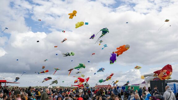 Das Bild zeigt Menschen und Drachen auf dem Tempelhofer Feld beim STADT UND LAND-Festival der Riesendrachen