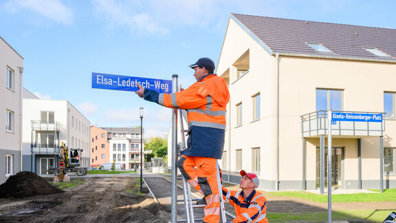 Zwei Mitarbeiter der Firma VSTR AG Rodewisch montieren die neuen Straßenschilder auf dem Gut Alt-Biesdorf