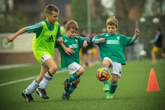 Auf dem Bild sind drei Jungs zu sehen, die Fußball spielen.