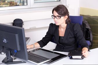 Das Bild zeigt eine junge Frau mit Brille vor einem PC.